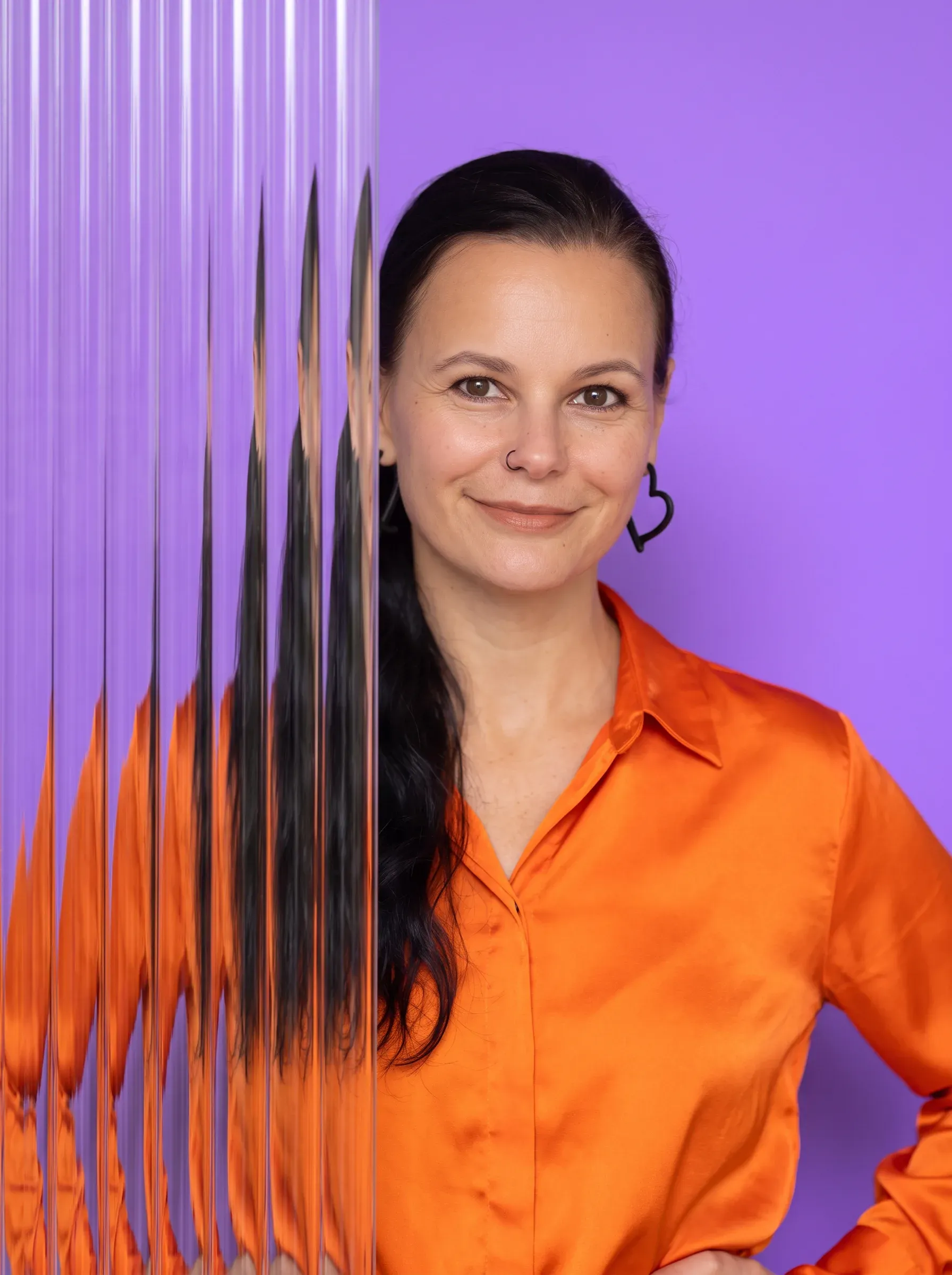 Porträt von Jenny in orangefarbener Bluse mit Riffelglas vor violettem Hintergrund