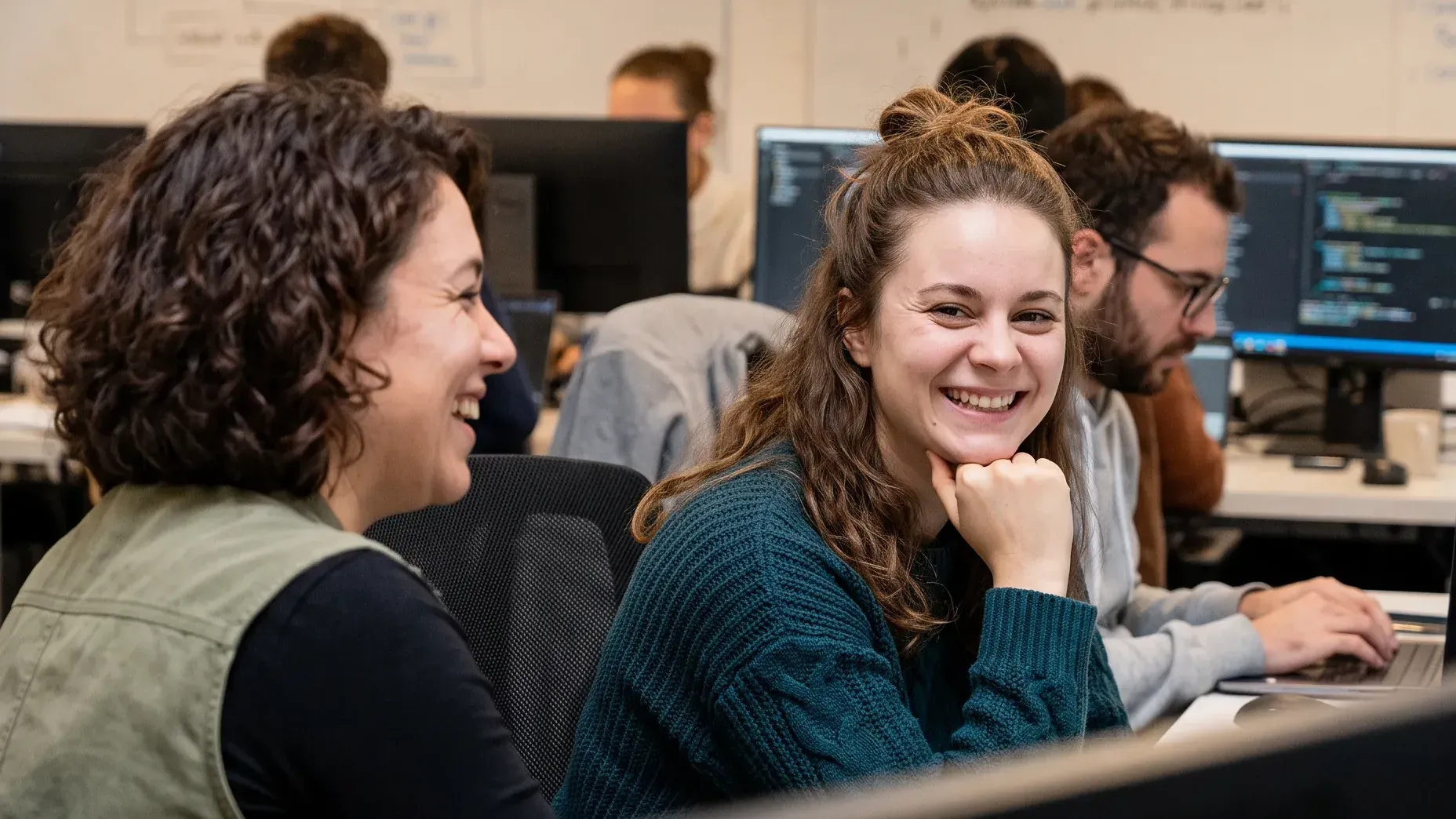 Team bei einem KI-Hackathon an den Rechnern, eine Teilnehmerin lacht in die Kamera