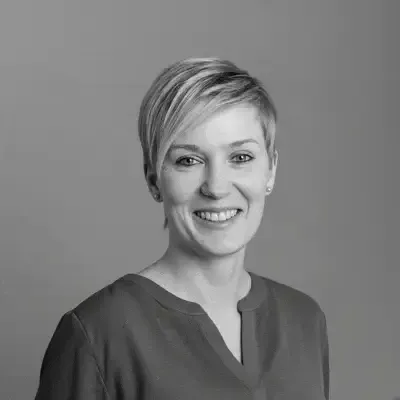 Schwarzweiss-Porträt einer lächelnden Frau mit kurzen blonden Haaren vor grauem Hintergrund
