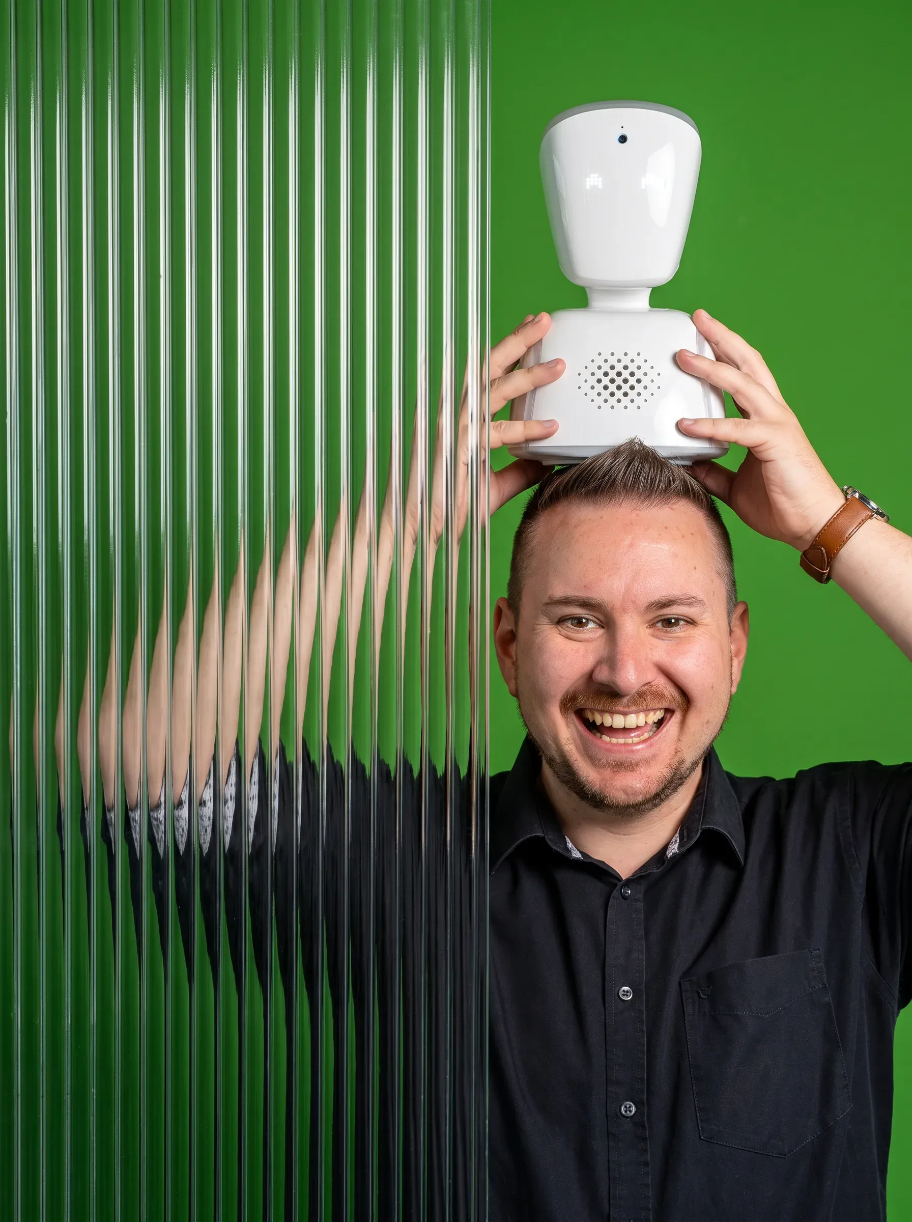 Georg Neumann vor grünem Hintergrund mit Riffelglas und kleinem weißen Roboter auf dem Kopf