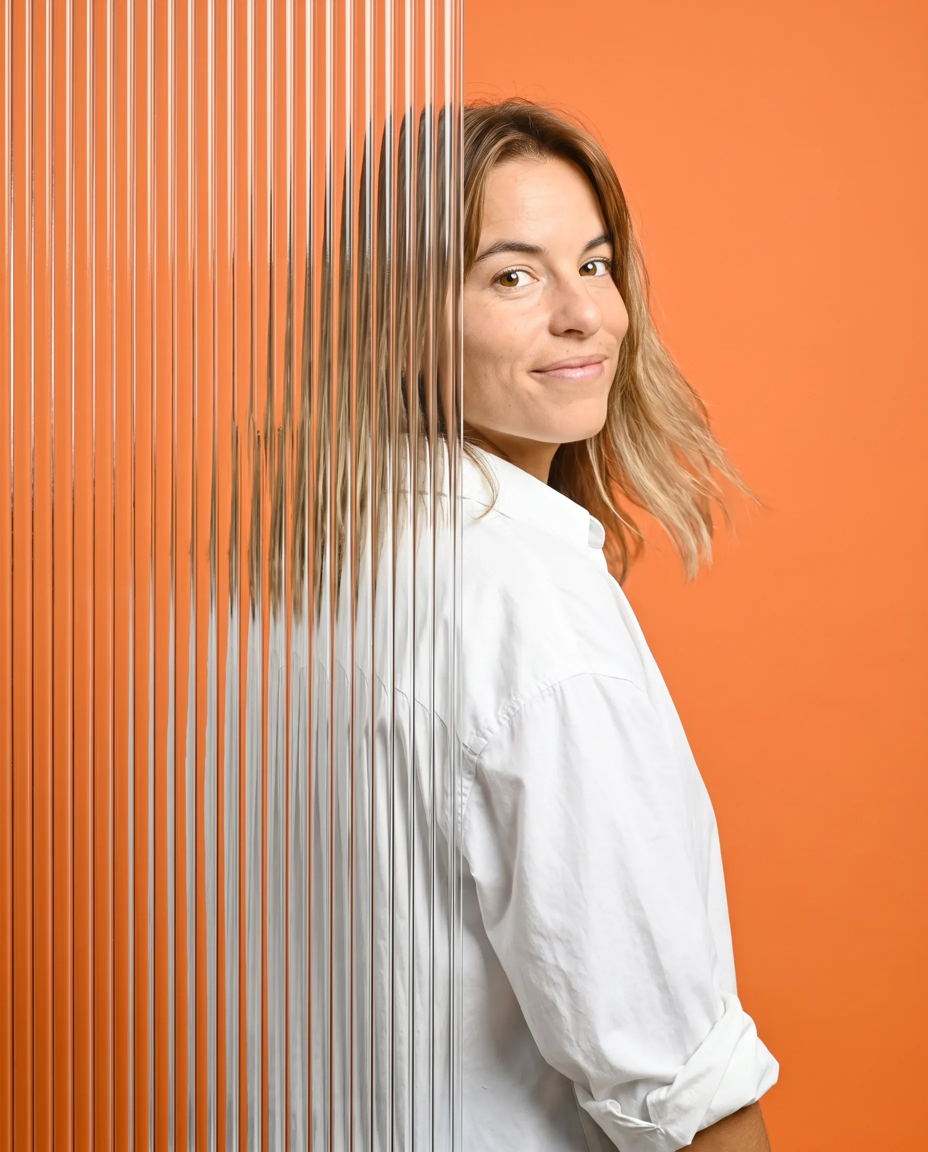 Kathi Kliem in weißer Bluse vor orangefarbenem Hintergrund neben Riffelglas